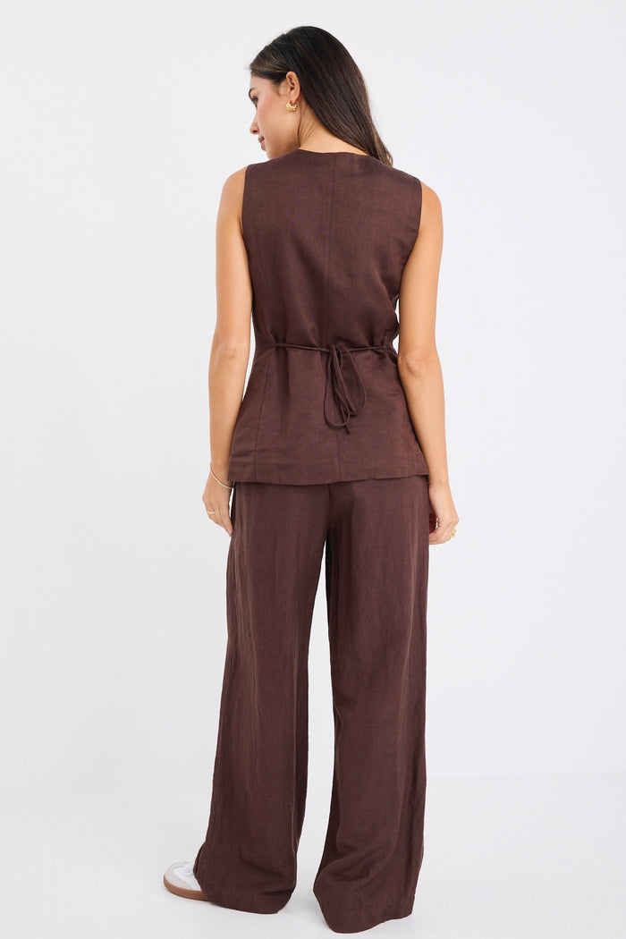 Woman wearing wide-leg chocolate brown trousers with a mid-rise waist.