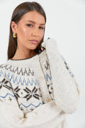 A woman wearing a cosy cream-colored cardigan with a Fair Isle pattern in shades of brown and blue, paired with high-waisted, relaxed-fit blue jeans.