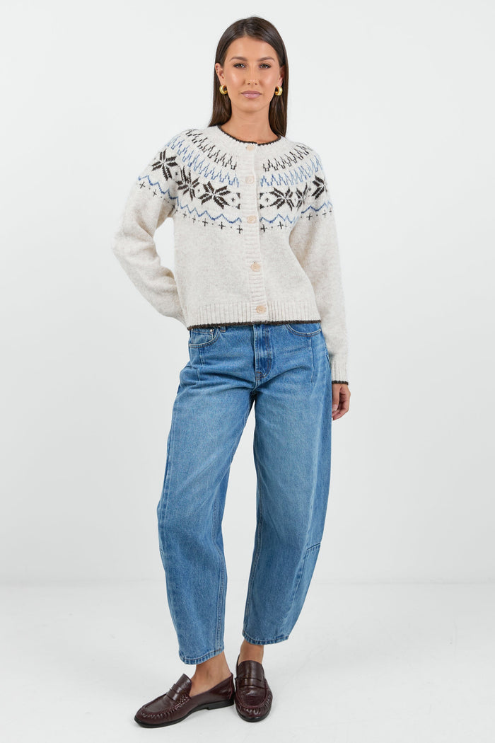 A woman wearing a cosy cream-colored cardigan with a Fair Isle pattern in shades of brown and blue, paired with high-waisted, relaxed-fit blue jeans.