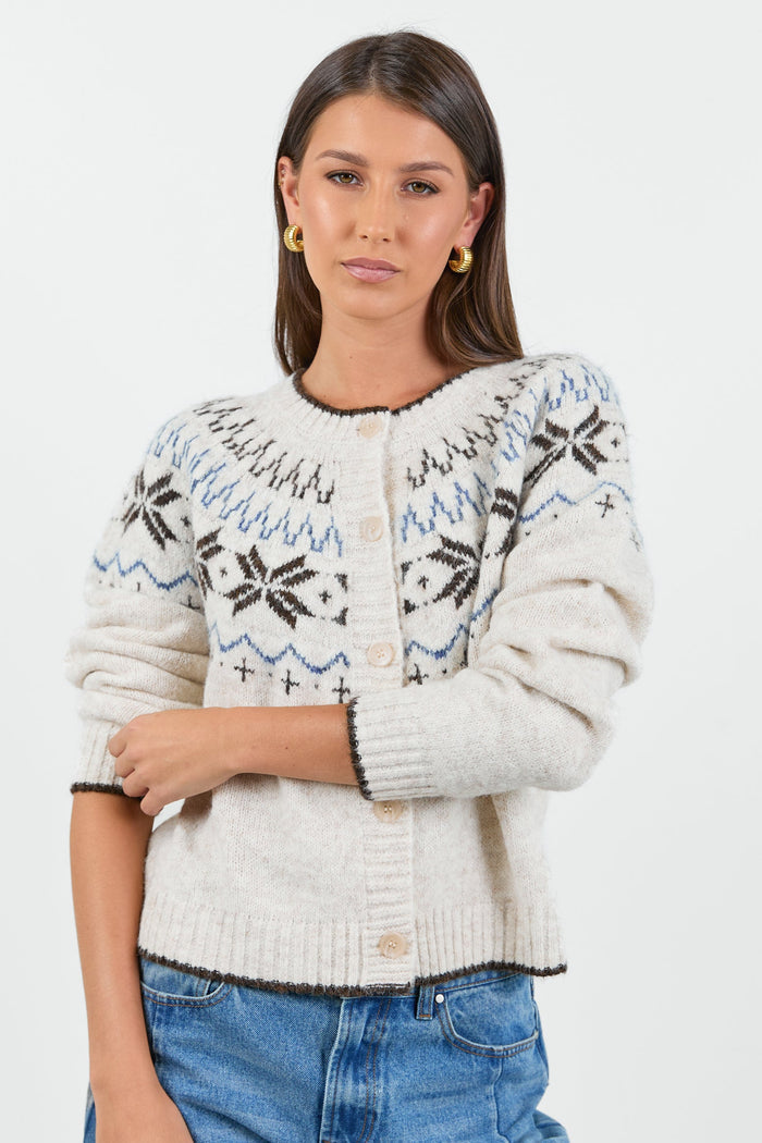 A woman wearing a cosy cream-colored cardigan with a Fair Isle pattern in shades of brown and blue, paired with high-waisted, relaxed-fit blue jeans.