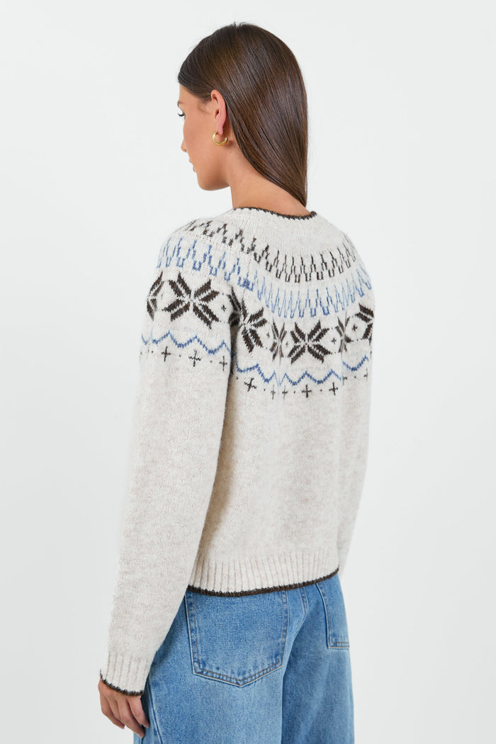 A woman wearing a cosy cream-colored cardigan with a Fair Isle pattern in shades of brown and blue, paired with high-waisted, relaxed-fit blue jeans.
col_pattern