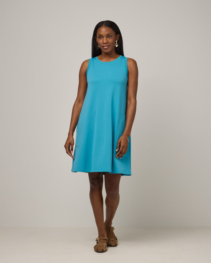 Model wearing Sierra Tank Dress in Sea Blue, a bright sky blue color. Sierra Tank Dress is a merino wool sleeveless, crew neck, knee length swing dress with pockets available in sizes XS-3X Regular, XS-3X Long, XS-XL Petite.