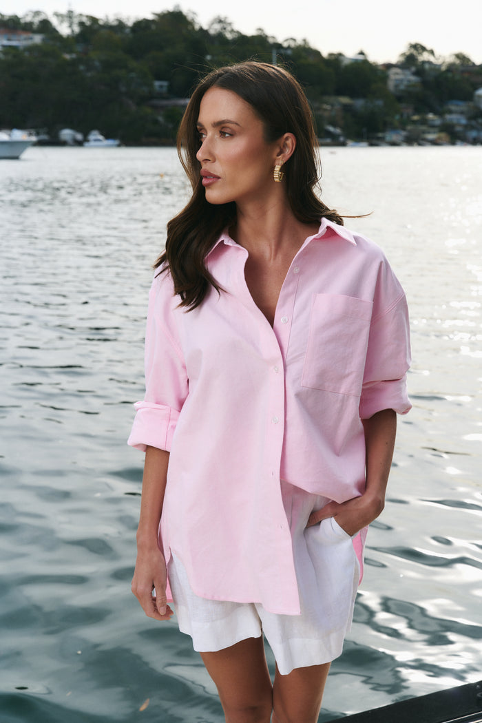 Woman wearing a pink shirt and white shorts by a body of water.