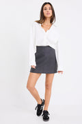 Woman wearing a dark charcoal grey mini skirt with a white oversized shirt and black sneakers, showing a clean, minimal outfit with street-style flair.