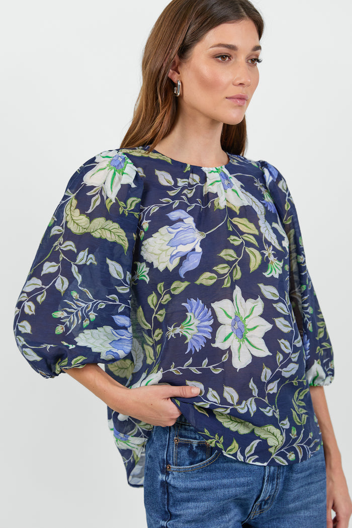 Close up of a woman wearing a floral blouse and blue jeans on a white background.