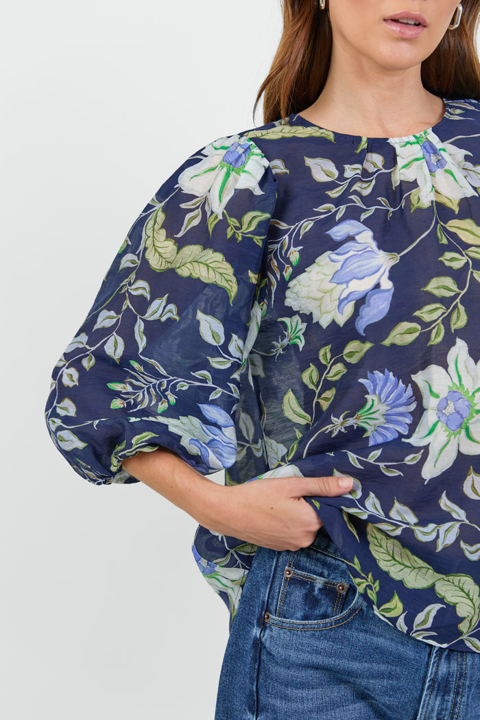 Close up of a woman wearing a floral blouse and blue jeans on a white background.