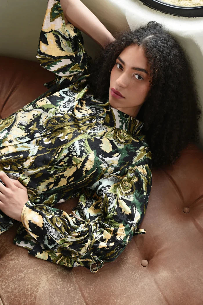 Woman in a patterned outfit sitting on a brown leather couch.