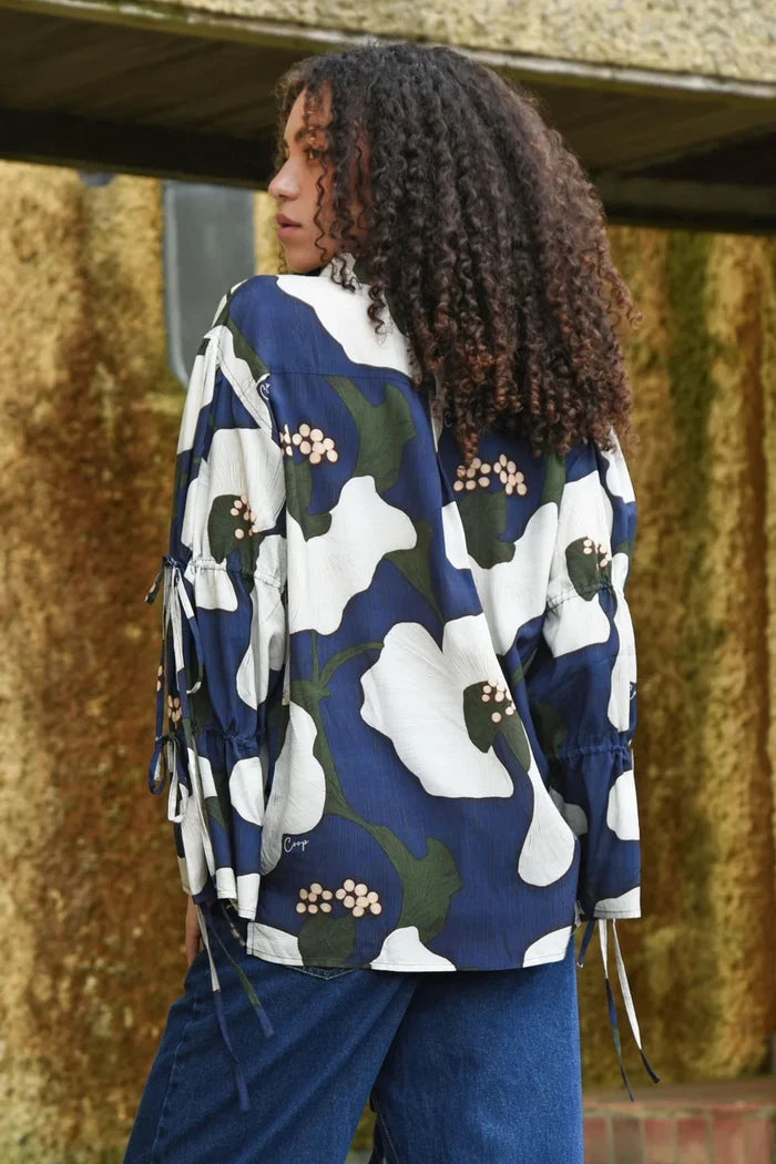Person wearing a blue floral patterned jacket with a backpack, standing against a textured wall.
