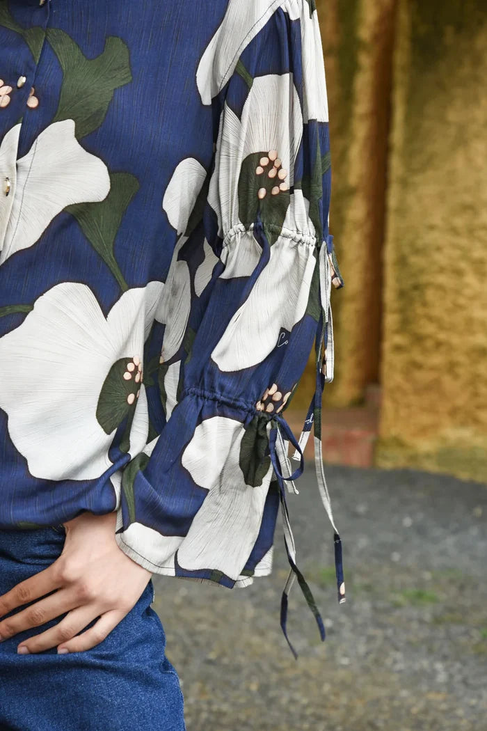 Close-up of a person wearing a blue floral dress with white flowers and green leaves.