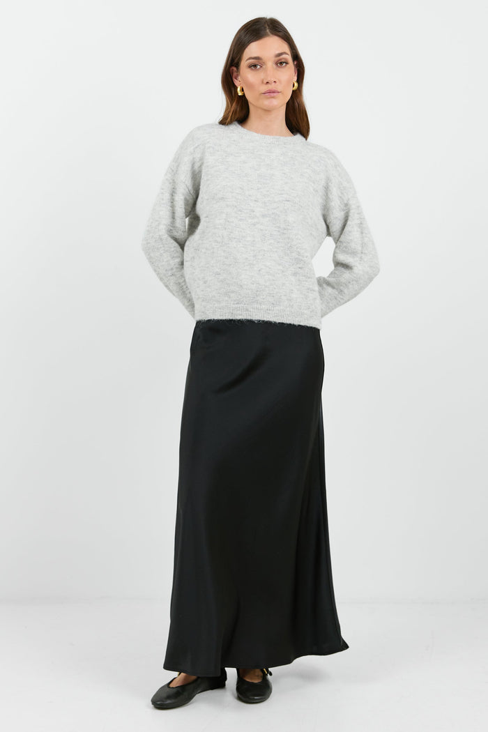 A woman wearing a light grey marle jumper with a relaxed fit and long sleeves. The sweater has a soft, cozy texture and a round neckline.