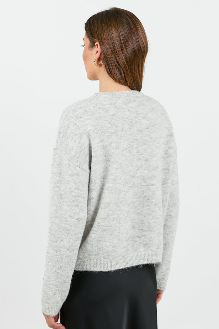 A woman wearing a light grey marle jumper with a relaxed fit and long sleeves. The sweater has a soft, cozy texture and a round neckline.