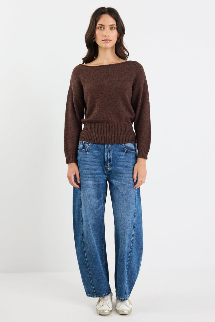 Woman wearing a brown sweater and blue jeans on a white background