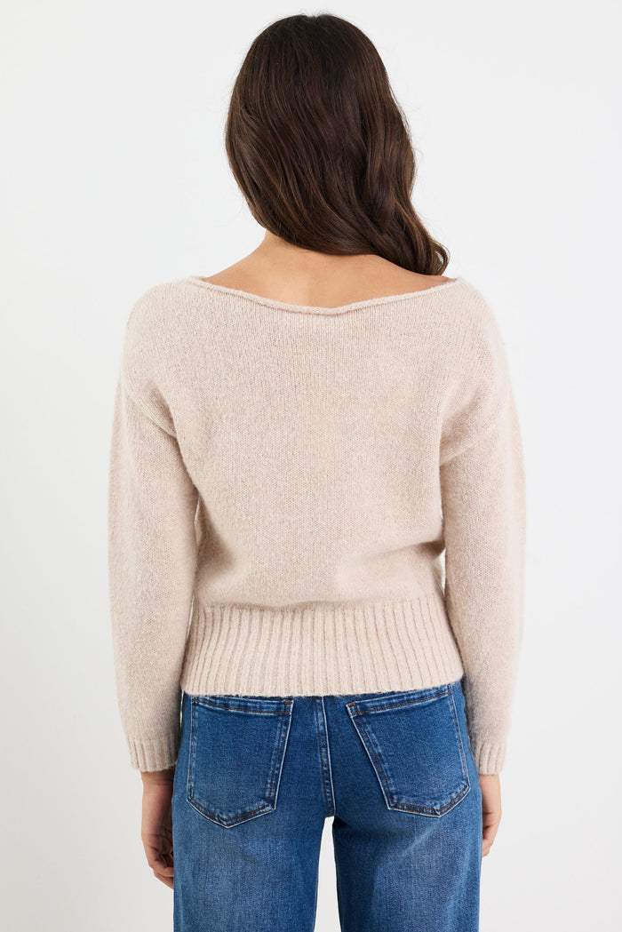 Person wearing a beige sweater and blue jeans on a white background