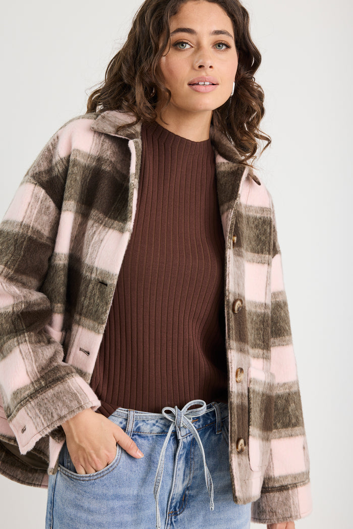Woman wearing a plaid shirt over a brown sweater with blue jeans on a white background