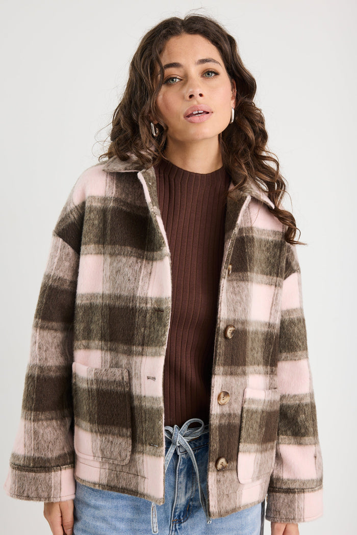 Woman wearing a plaid jacket over a brown top and blue jeans on a white background