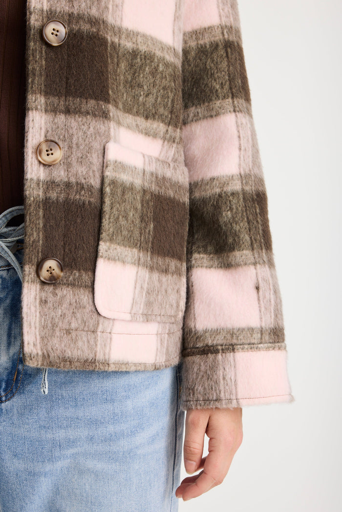 Plaid jacket with buttons and a pocket, worn over jeans on a plain background