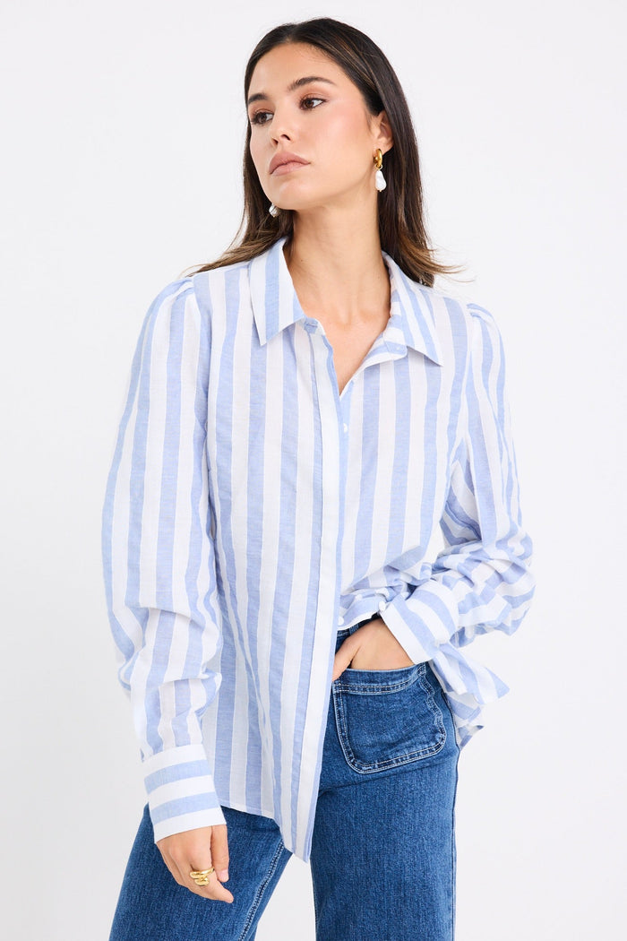 Woman wearing a relaxed blue and white vertical stripe shirt with balloon sleeves, styled casually with wide-leg blue jeans.