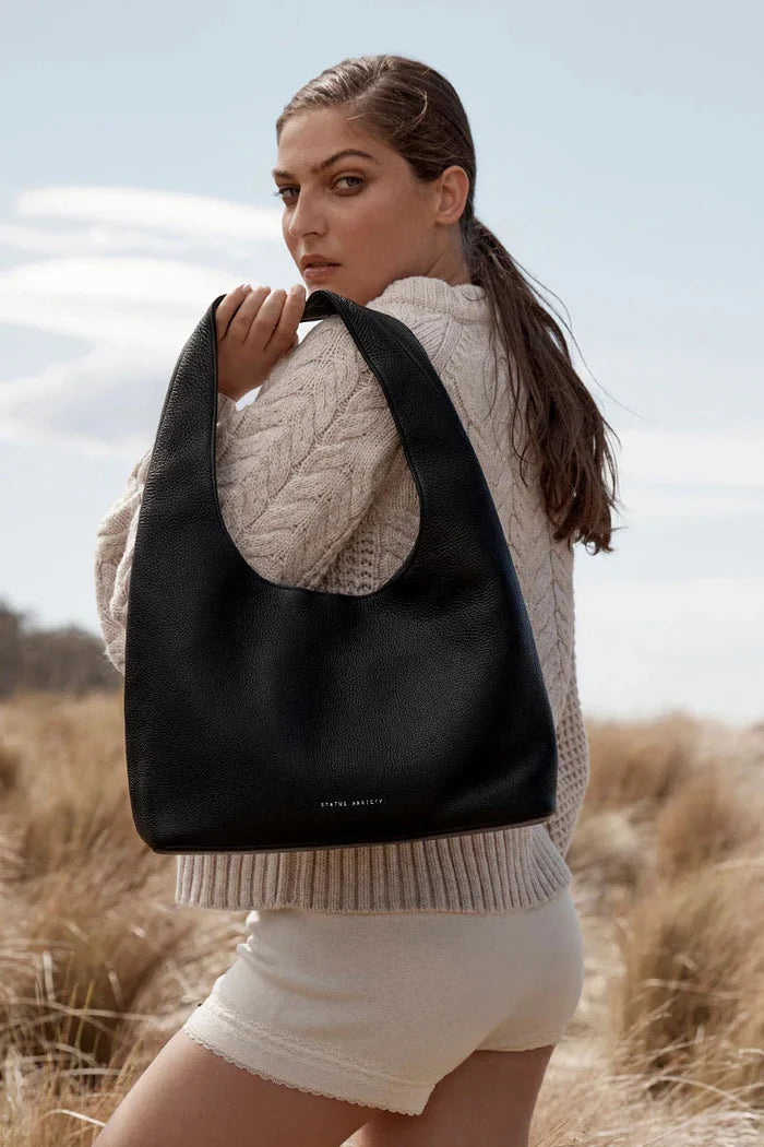Woman holding a black bag in a field with a neutral background