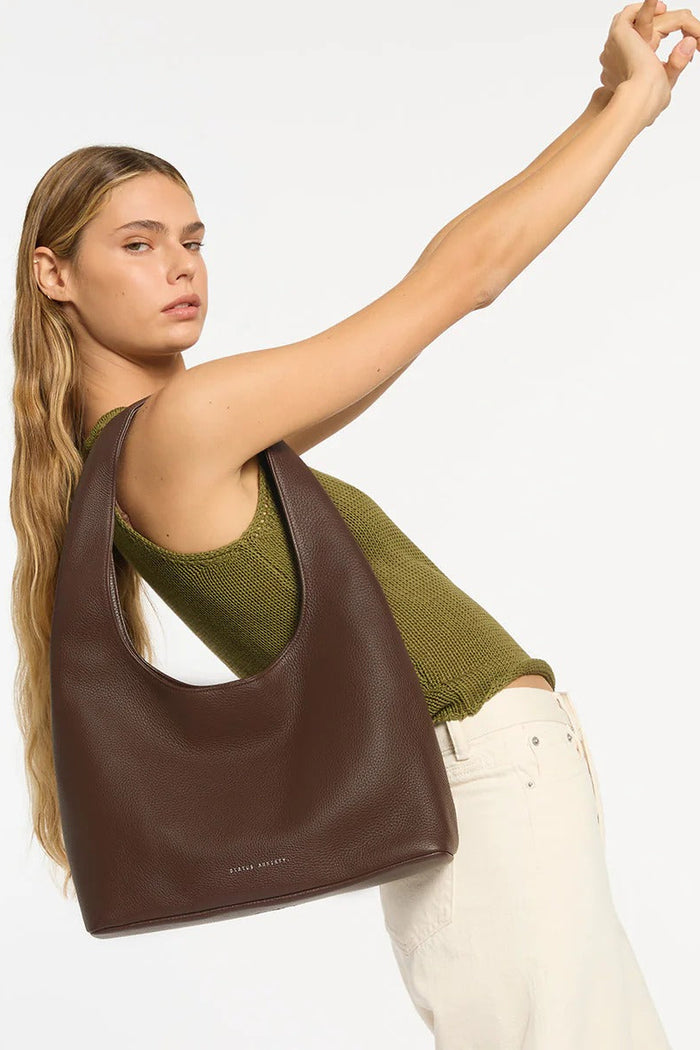 Woman holding a brown leather bag against a white background