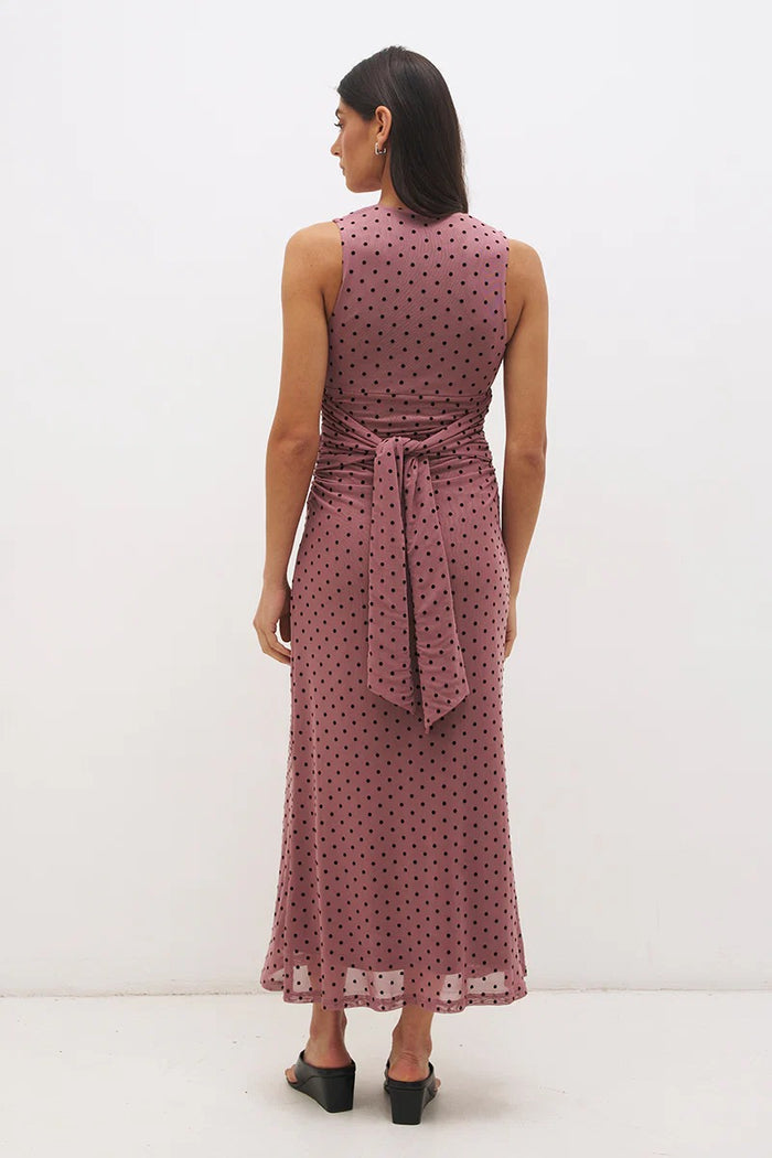 Woman wearing a sleeveless, polka-dotted dress with a belt on a white background
