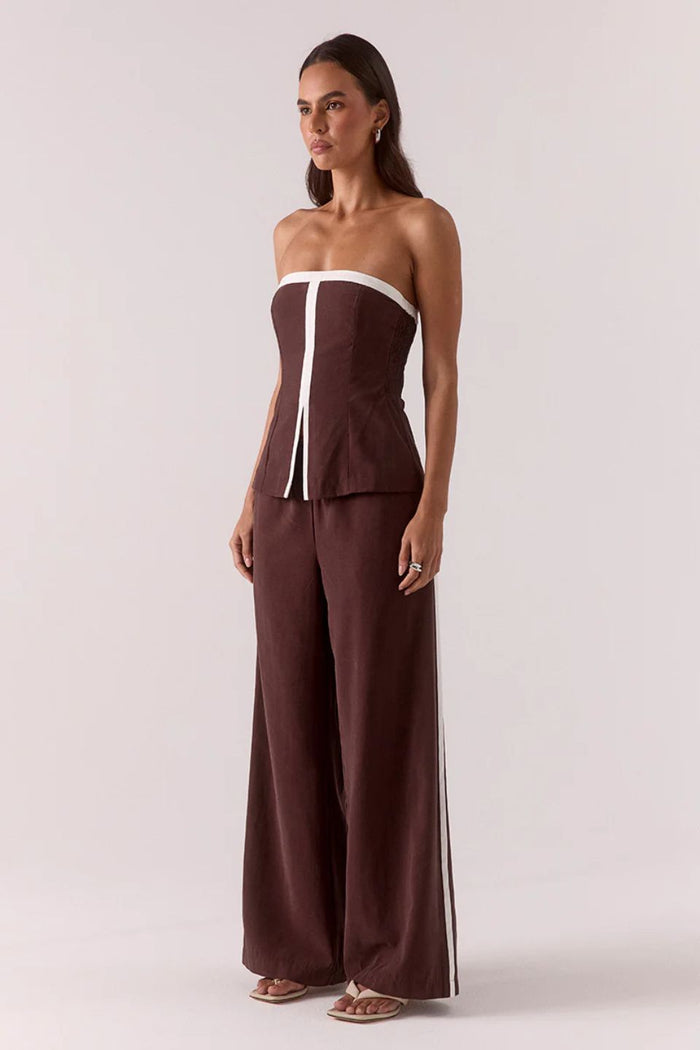 Woman wearing a brown strapless jumpsuit with white accents on a plain background