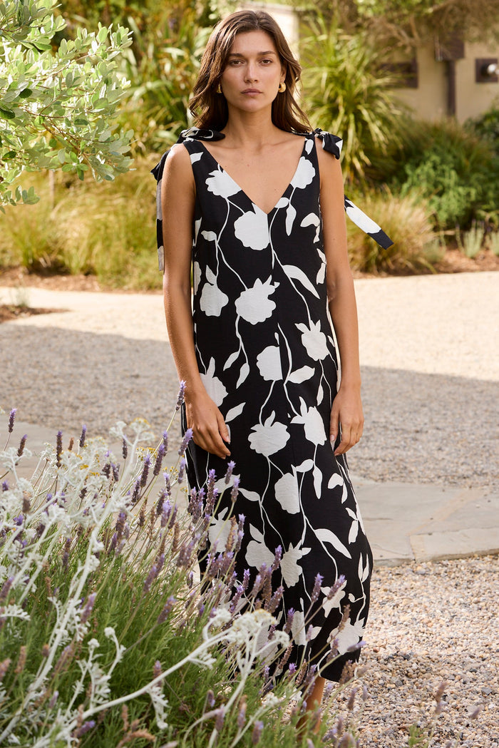 Woman in a black and white floral dress standing in a garden.
