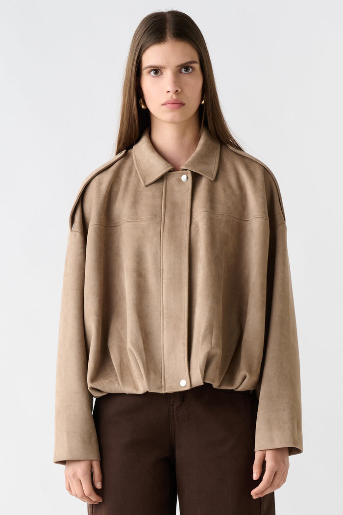 Woman wearing a beige jacket and brown pants on a white background