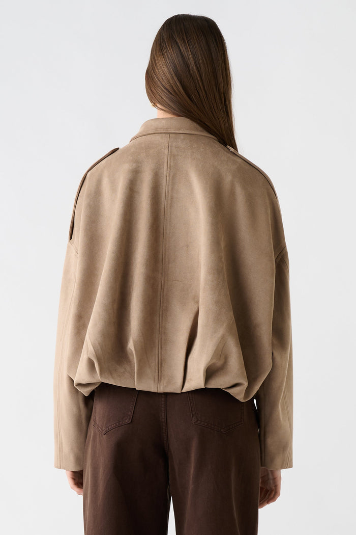 Person wearing a beige jacket and brown pants on a white background