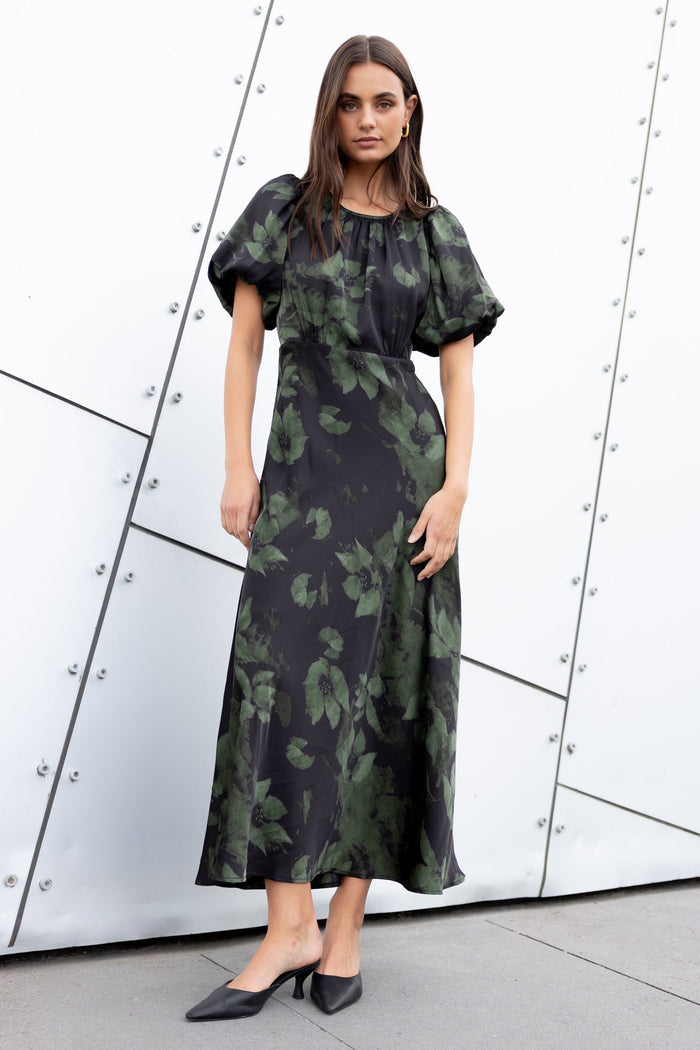 Woman wearing a green floral dress against a modern architectural background