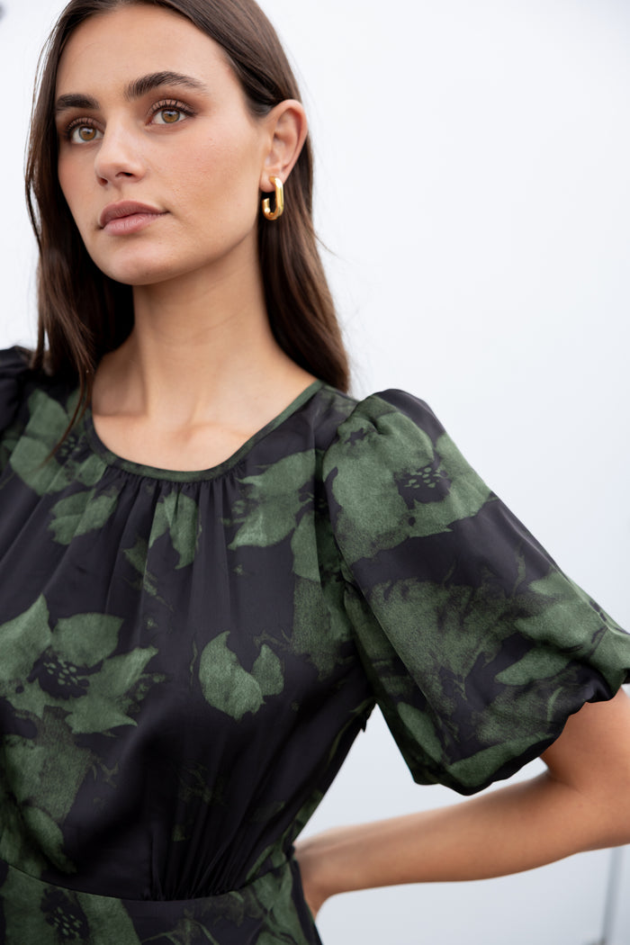 Woman wearing a dark green floral blouse against a white background