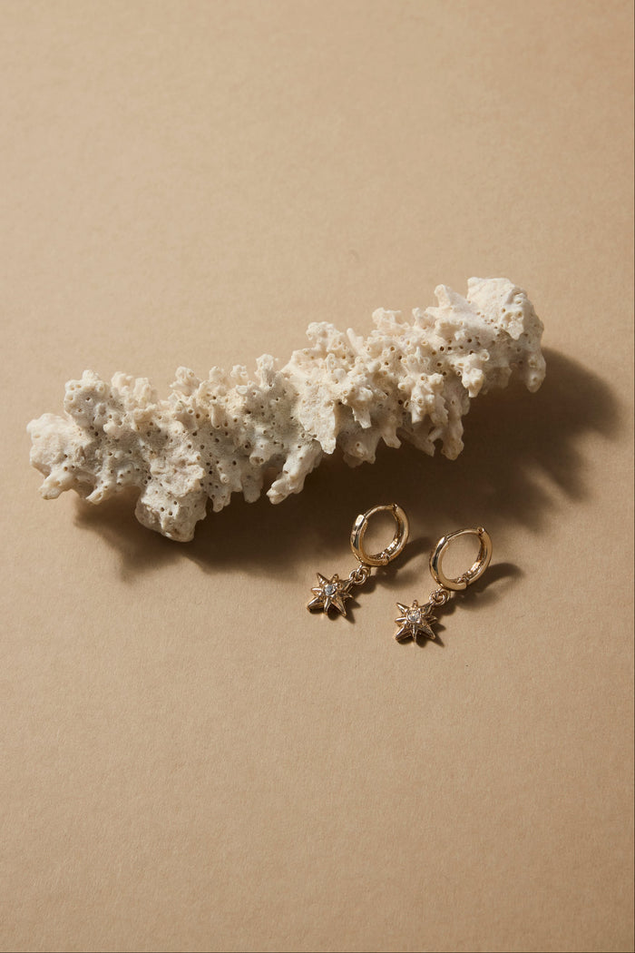 Gold earrings on a beige surface with a white textured object