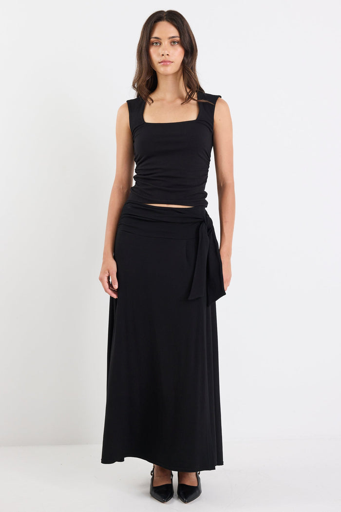 Woman wearing a black sleeveless top and long black skirt on a white background