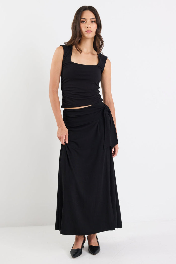 Woman wearing a black sleeveless top and long skirt on a white background
