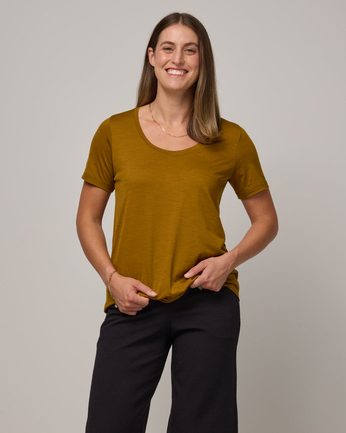 Model wearing Stella Scoop Neck Tee in Spiced Pear, a dark mustard color. Stella Scoop Neck Tee is a merino wool short sleeve, scoop neck t-shirt available in sizes XS-3X.