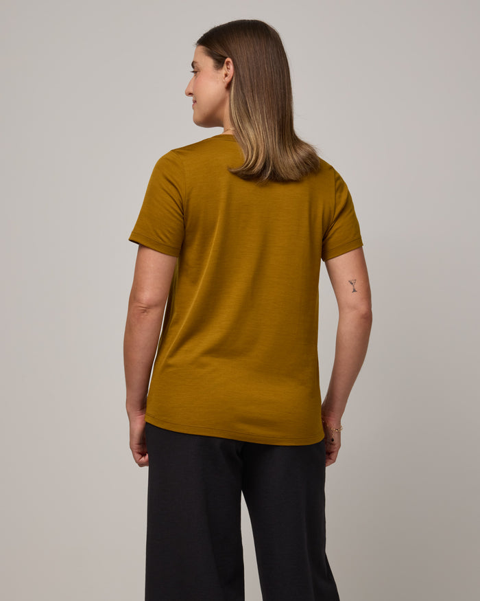 Model wearing Stella Scoop Neck Tee in Spiced Pear, a dark mustard color. Stella Scoop Neck Tee is a merino wool short sleeve, scoop neck t-shirt available in sizes XS-3X.