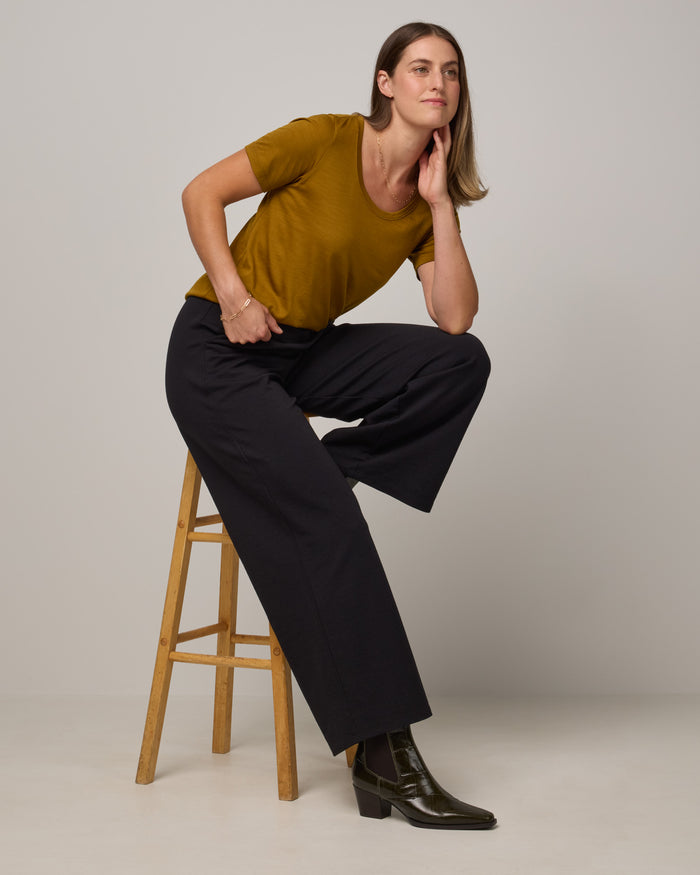Model wearing Stella Scoop Neck Tee in Spiced Pear, a dark mustard color. Stella Scoop Neck Tee is a merino wool short sleeve, scoop neck t-shirt available in sizes XS-3X.