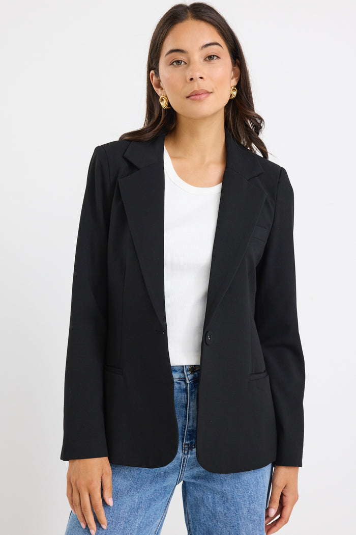 model wears a black fitted blazer and blue wide leg jean