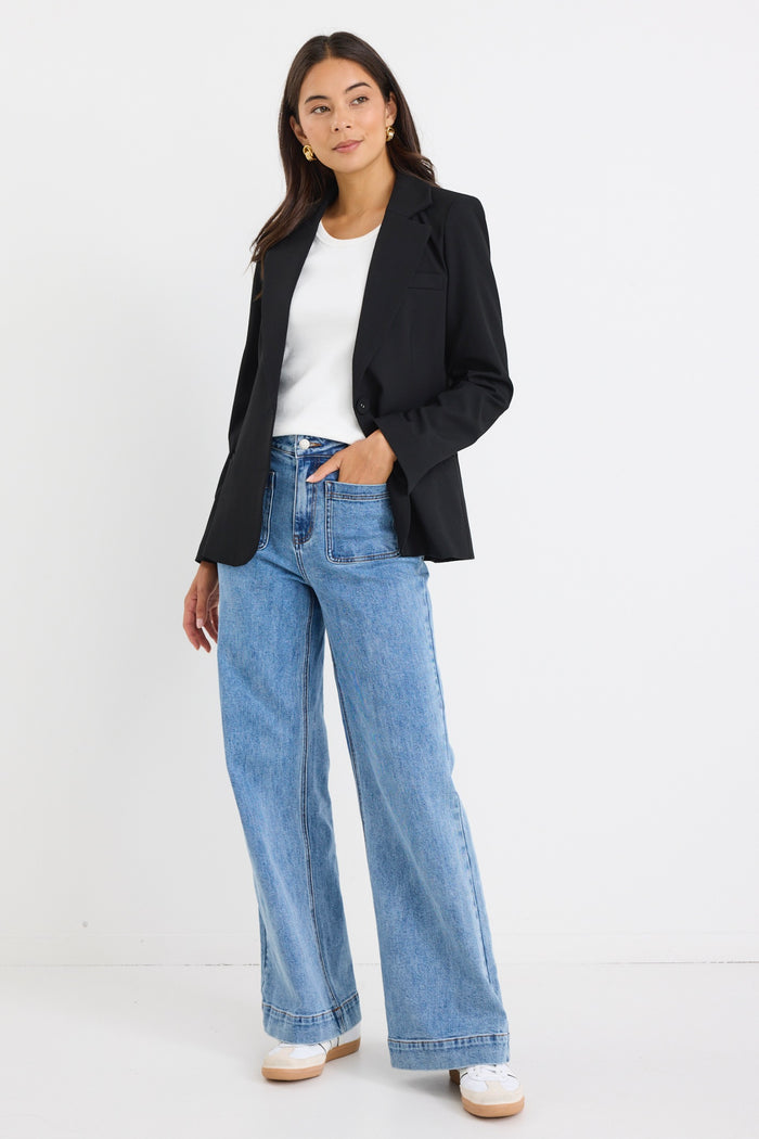 model wears a black fitted blazer and blue wide leg jean