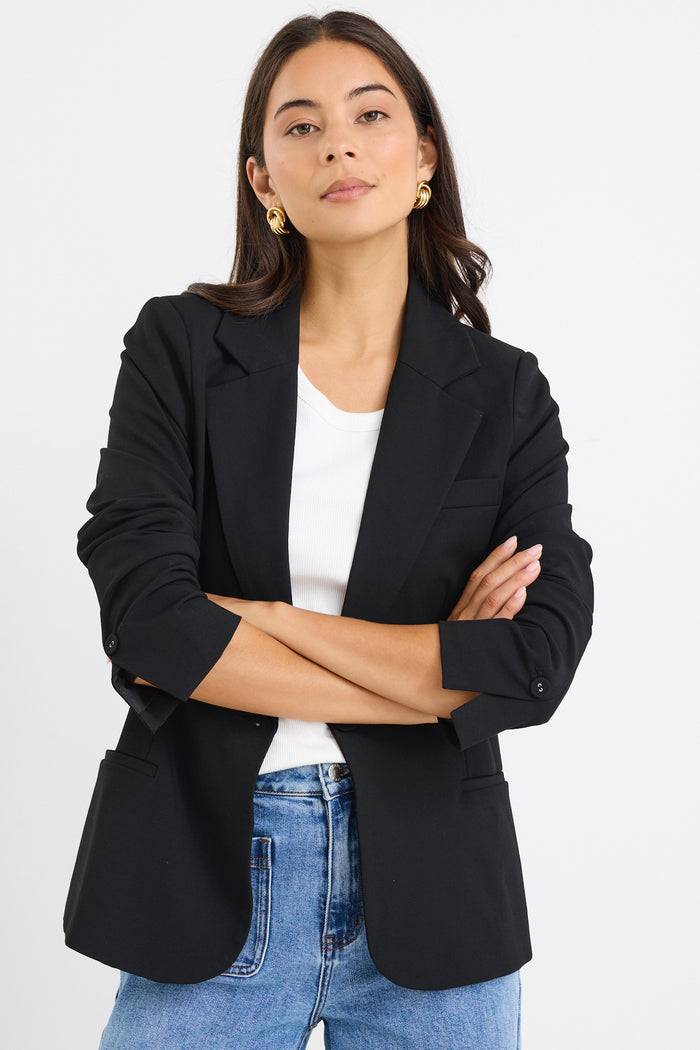 model wears a black fitted blazer and blue wide leg jean