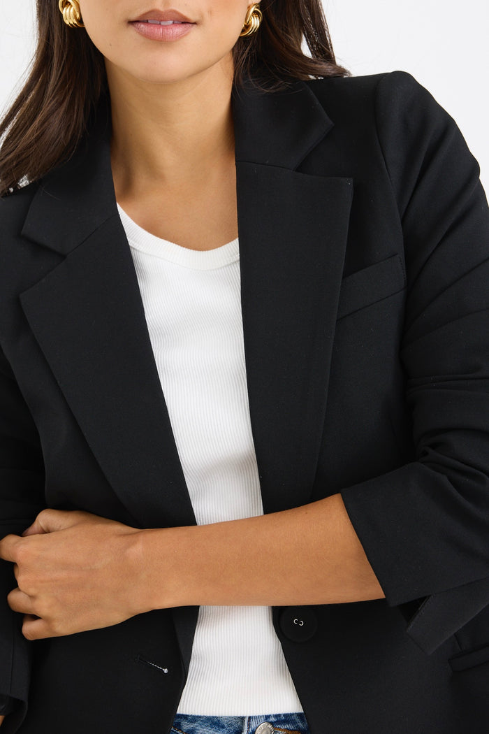 model wears a black fitted blazer and blue wide leg jean