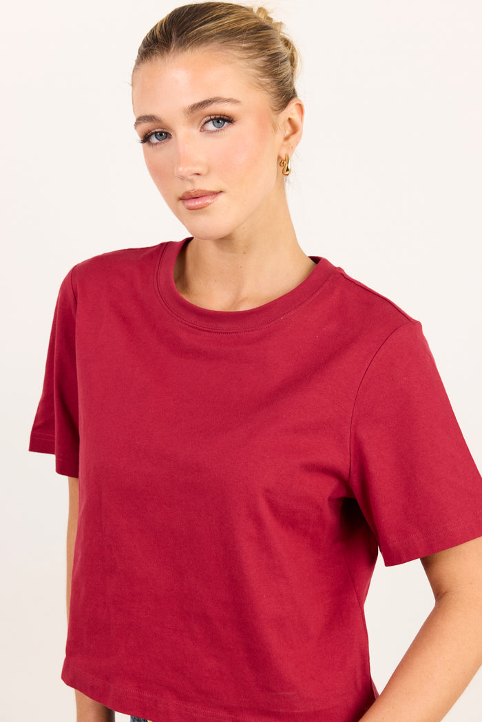 A woman wearing a short-sleeve crewneck t-shirt in a deep red color, photographed against a plain off-white background.