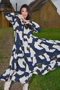 Woman wearing a long, patterned dress outdoors with a rustic building in the background