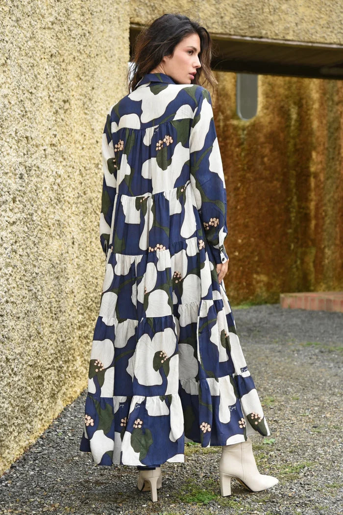 Woman wearing a long, patterned dress standing against a textured wall.
