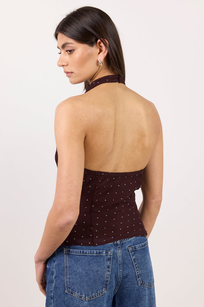 A woman shown from the back wearing a dark brown halter top with small white polka dots and blue jeans, photographed against a plain light background.
