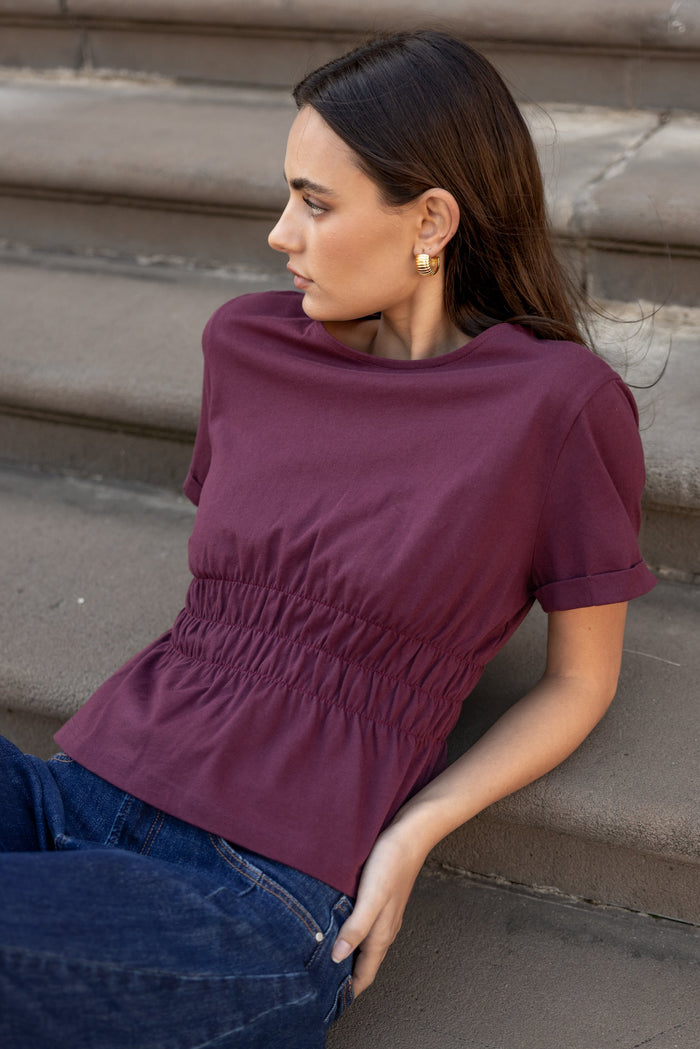 Woman wearing a purple top and blue jeans sitting on steps.