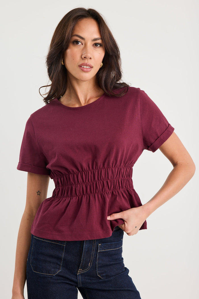 Woman wearing a maroon top and dark jeans on a white background