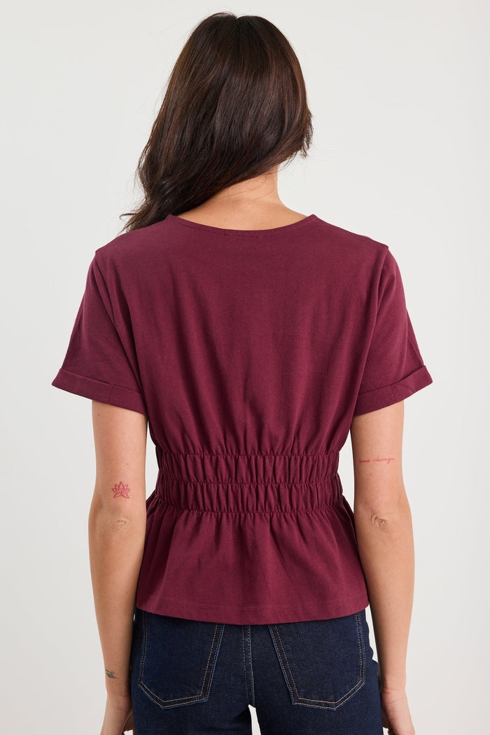 Person wearing a maroon top with a plain background