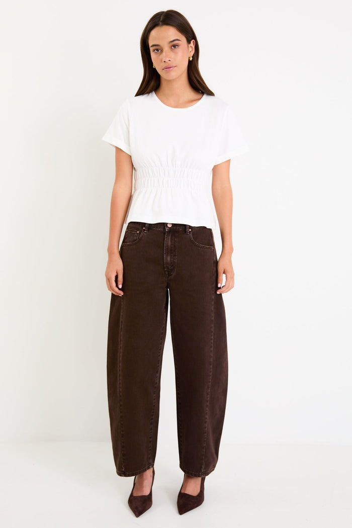 Woman wearing a white top and brown pants against a white background