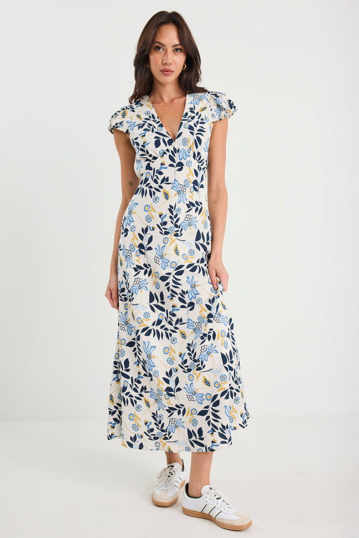 Woman wearing a floral dress with white sneakers on a plain background
