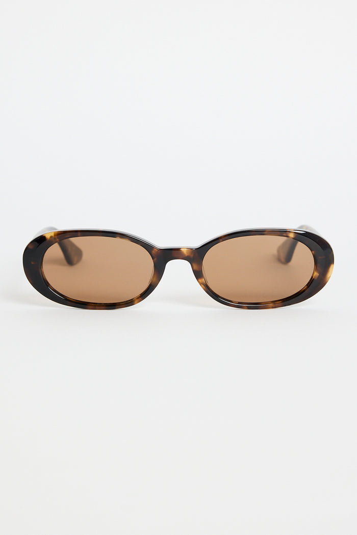 Narrow tortoiseshell oval sunglasses with warm brown tinted lenses, photographed against a white background